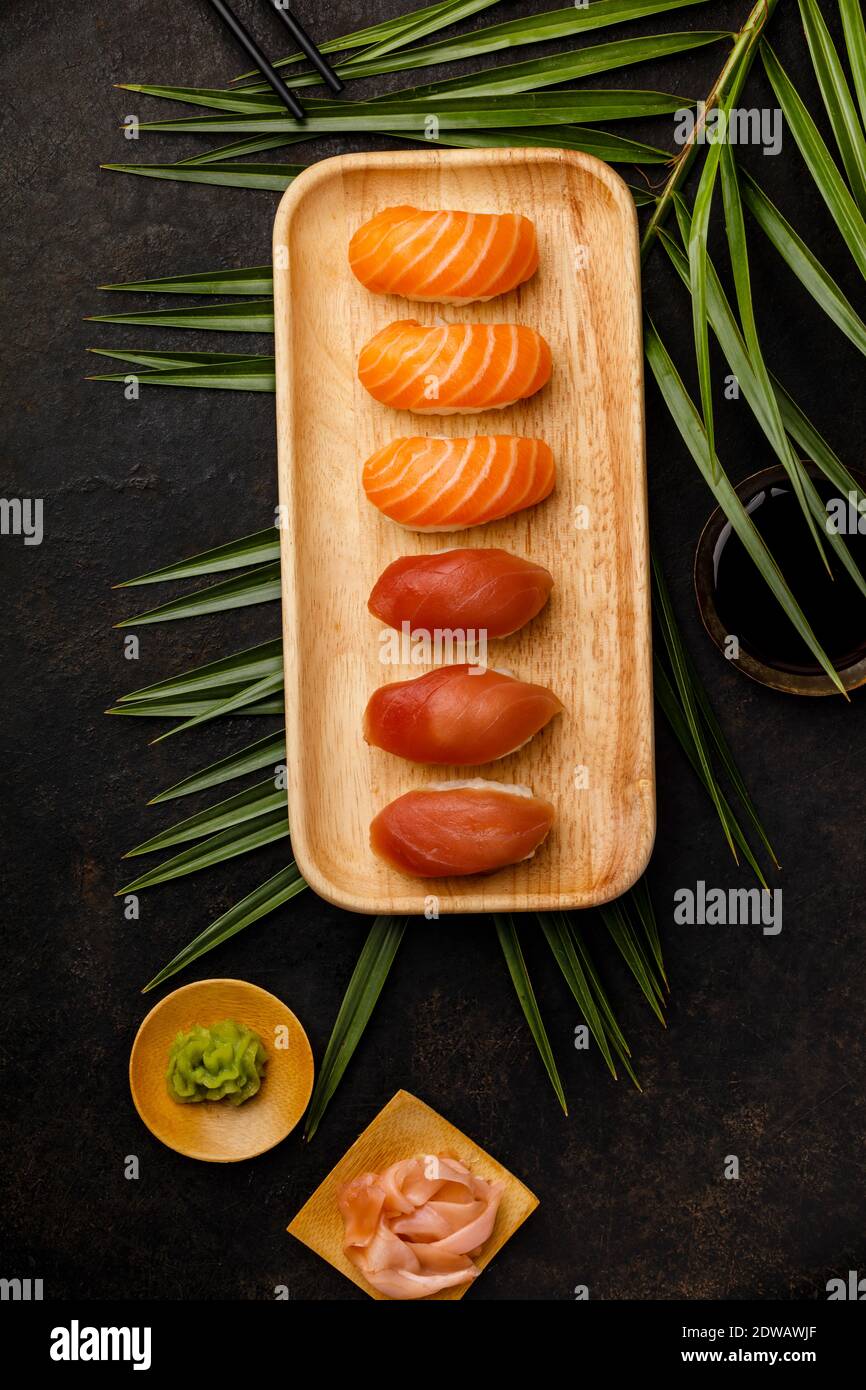 Nigiri sushi set with salmon and tuna served on bamboo plate with chopsticks, soy sause, wasabi, ginger and tea on dark background. Delicious traditio Stock Photo