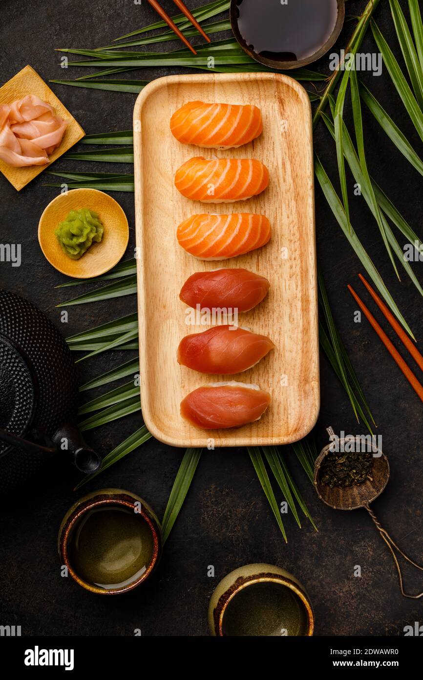 Nigiri sushi set with salmon and tuna served on bamboo plate with chopsticks, soy sause, wasabi, ginger and tea on dark background. Delicious traditio Stock Photo