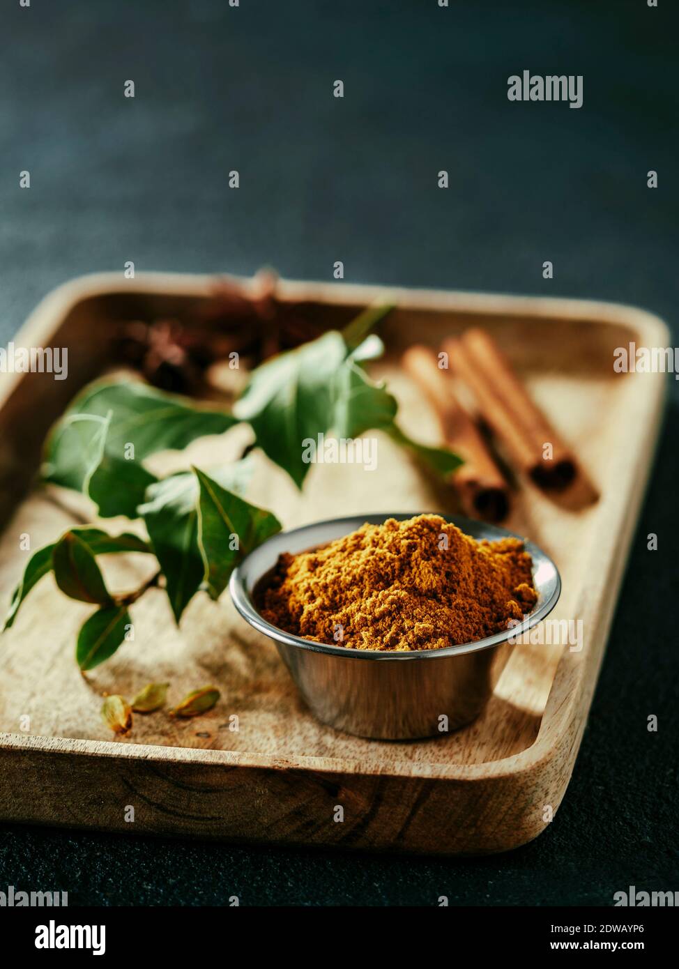 Indian or pakistani masala powder and spices on wooden tray. Small metall bowl with dry curry garam masala mix spices blend, green bay leaf, cinnamon Stock Photo