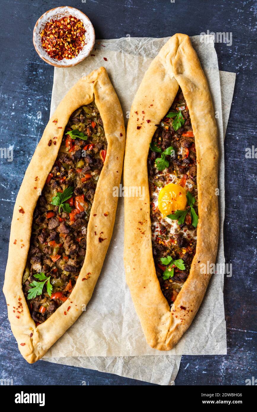 Turkish pide stuffed with beef and an egg photographed on a piece of baking paper on a dark background. Stock Photo