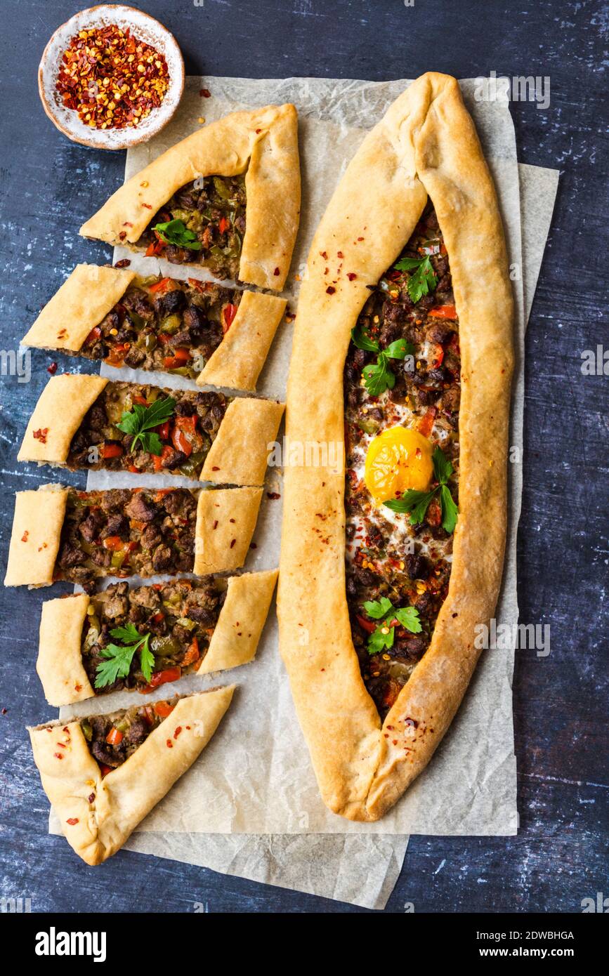 Turkish pide stuffed with beef and an egg photographed on a piece of baking paper on a dark background. Stock Photo