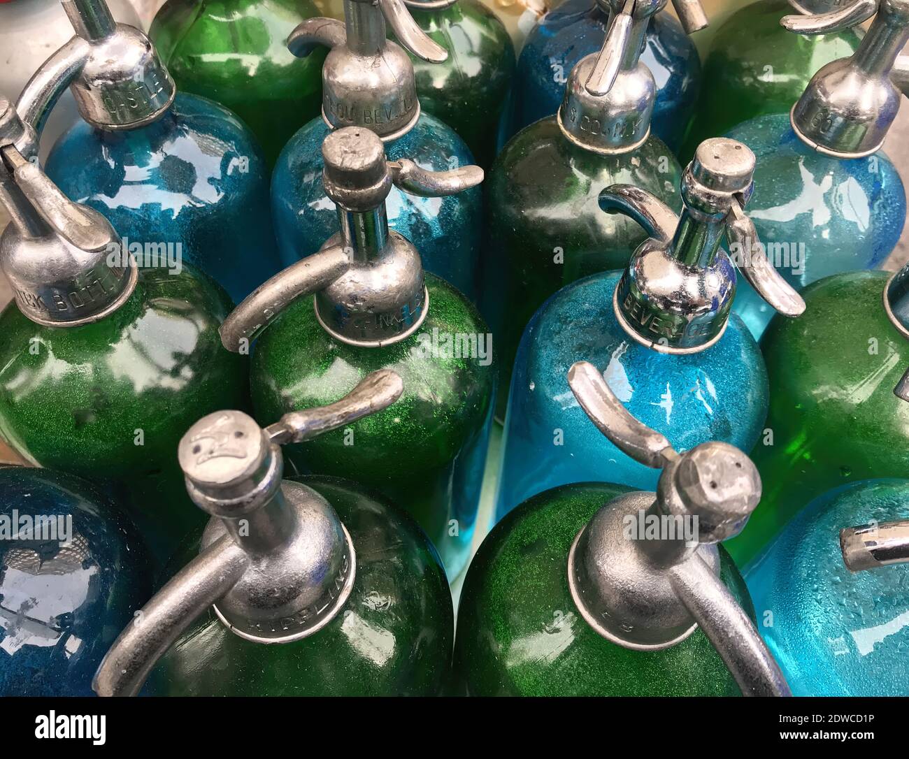 A photograph of a collection of blue and green glass antique seltzer bottles. Stock Photo