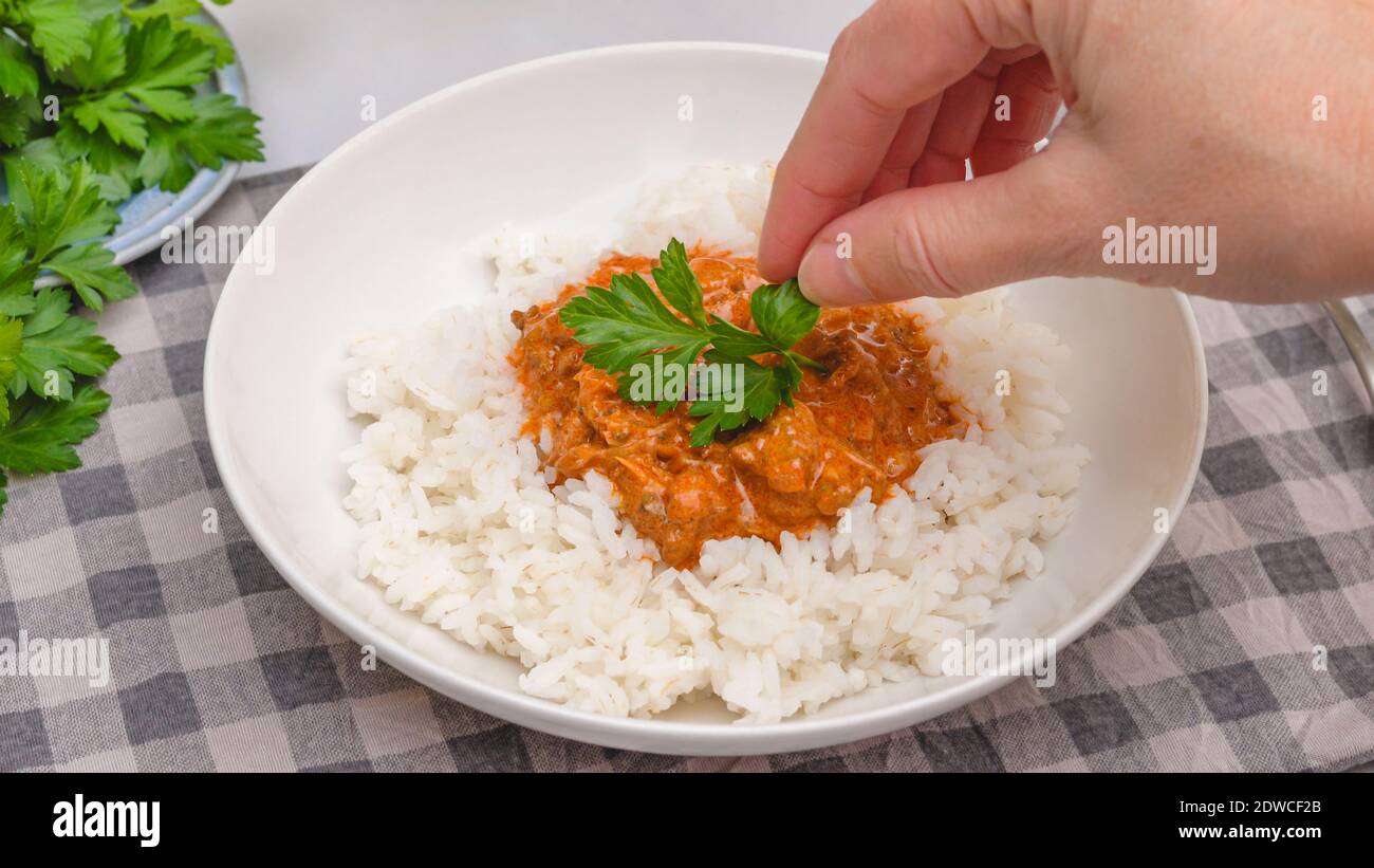 Hangarian paprikash, sour cream chicken paprika,  with rice and fresh parsley. Woman serving meal Stock Photo