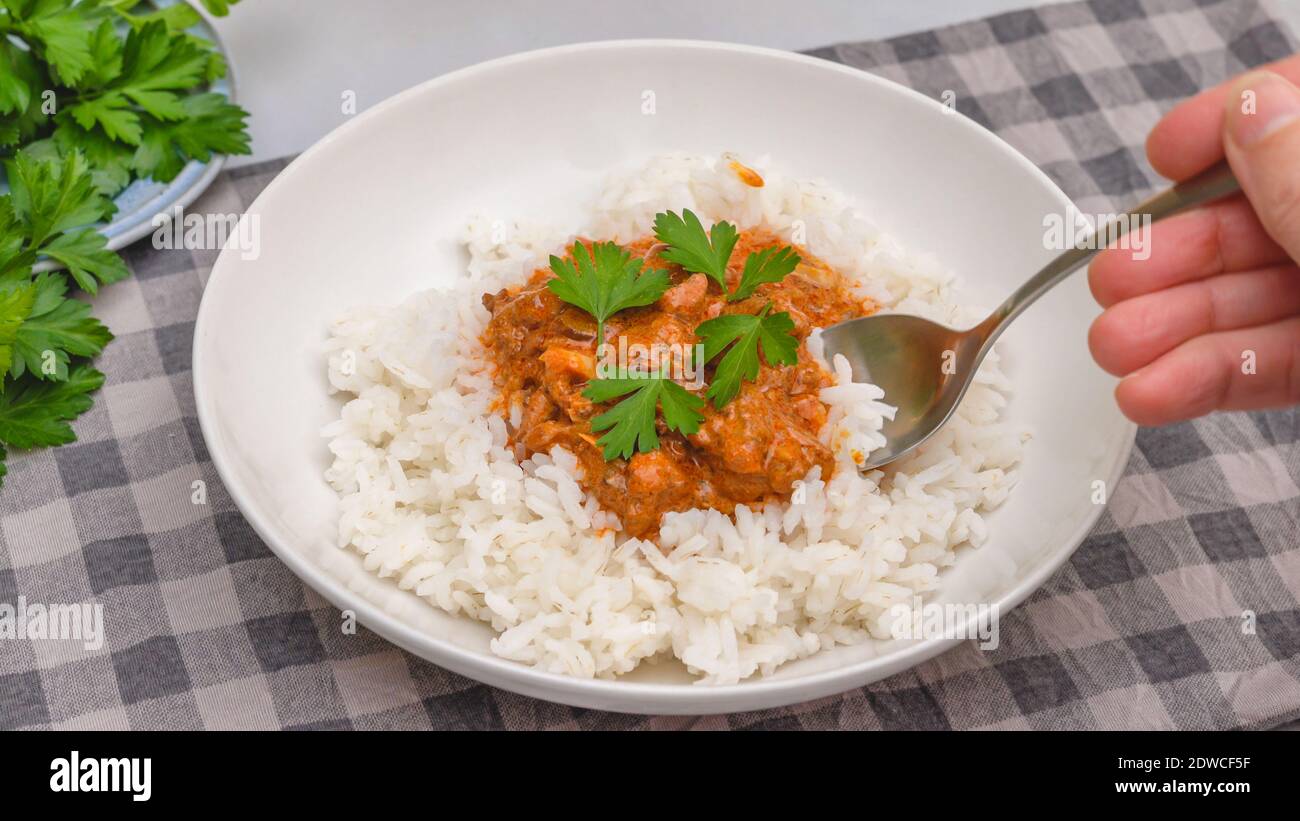 Delicious sour cream chicken paprika served with rice and fresh parsley close up on a plate on kitchen table Stock Photo