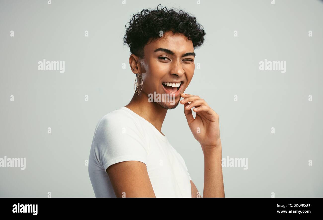 Gender fluid man with earring winking to the camera. Happy young guy winking  against white background. Stock Photo