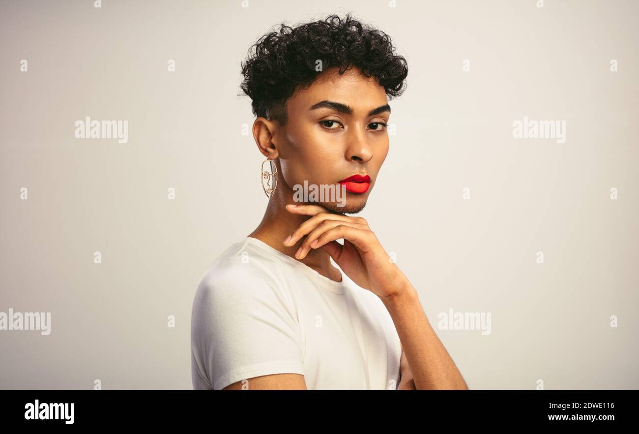 Portrait of a handsome gay man with make up. Transgender male with red lip stick and earring looking at camera. Stock Photo