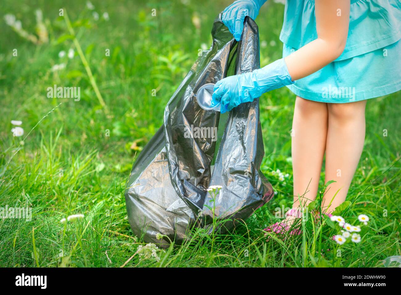 https://c8.alamy.com/comp/2DWHW90/childs-hand-puts-plastic-debris-in-the-garbage-bag-in-the-park-2DWHW90.jpg