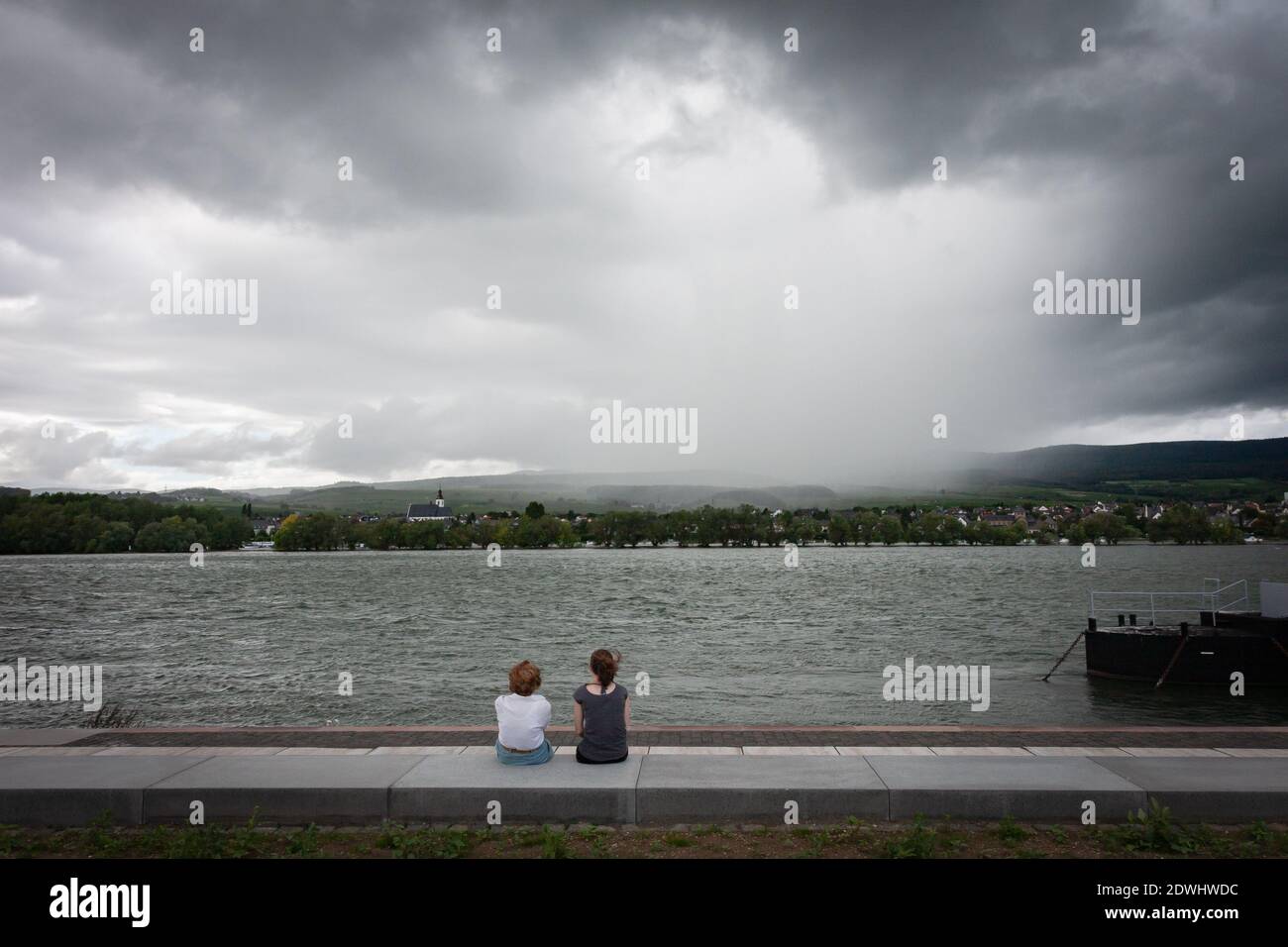 Rear View Of People Sitting By Lake Against Sky Stock Photo