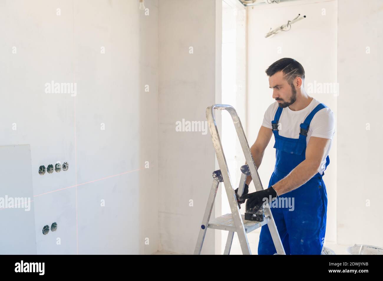 A foreman in overalls marks the wall using a laser level Stock Photo