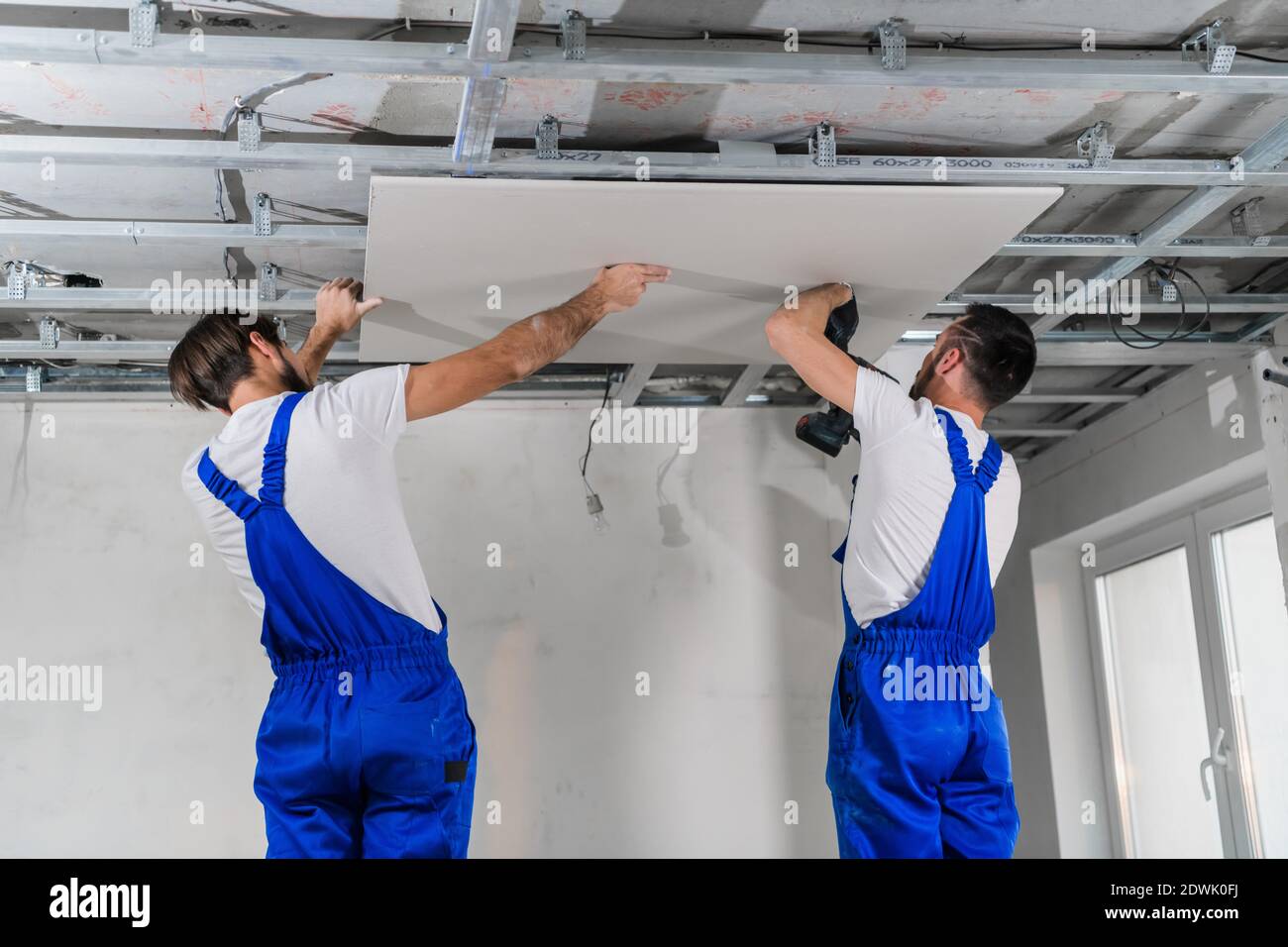 Builders in blue overalls stand on a ladder and make a ceiling Stock Photo