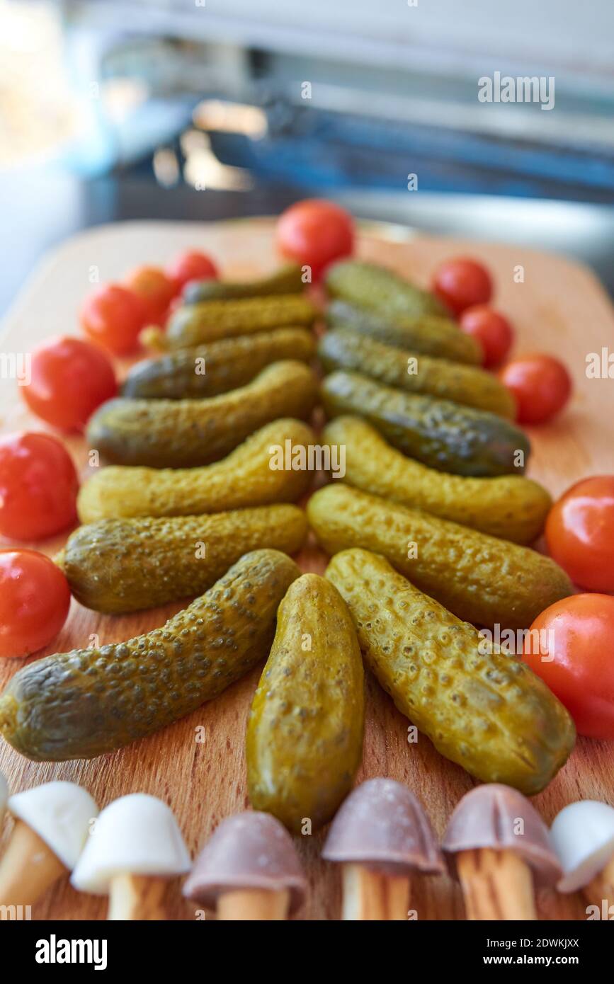 Christmas tree made of pickled cucumbers, decorated with cherry tomatoes, sweet mushroom-shaped cookies below Stock Photo