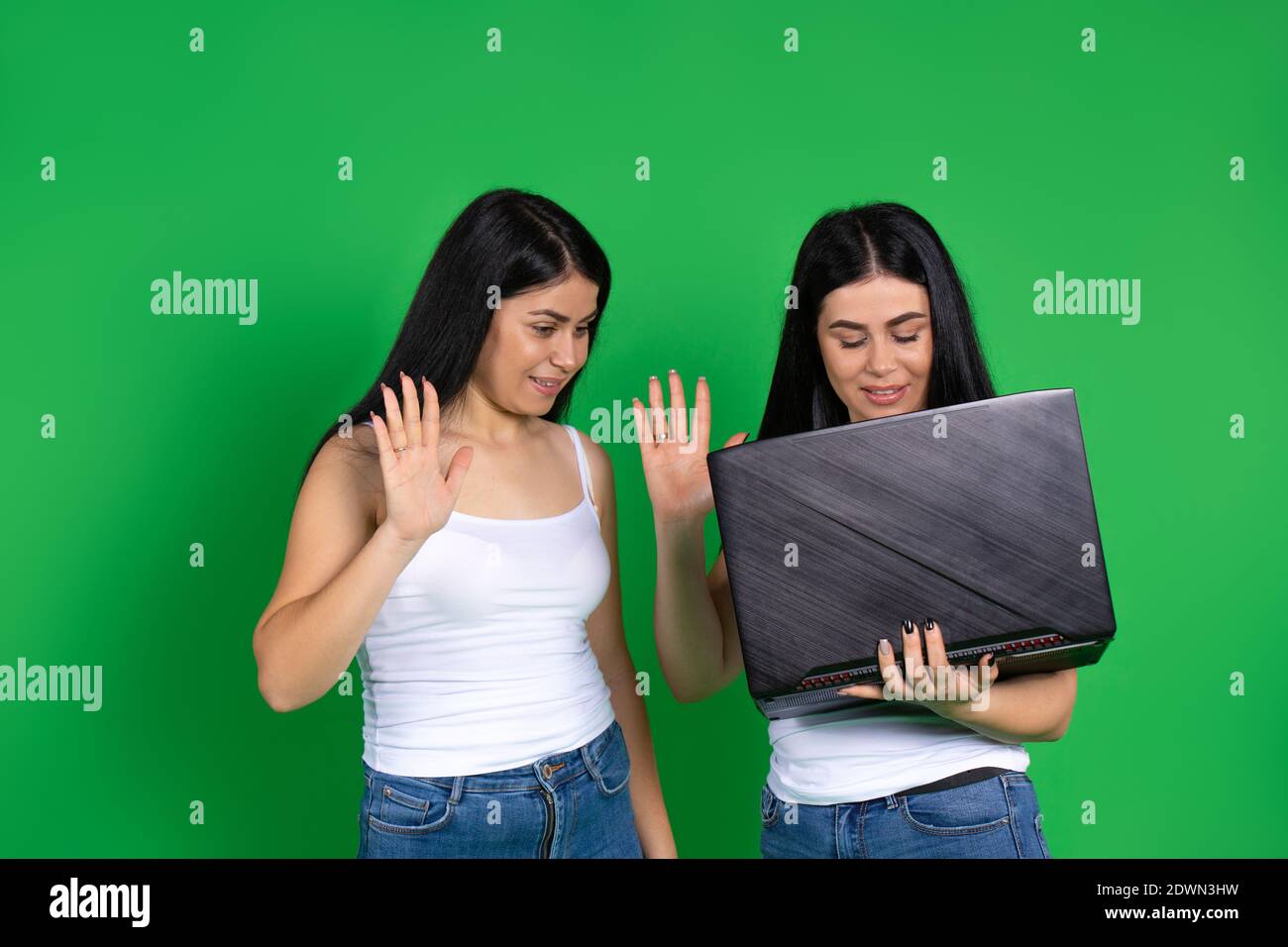 Twin girls on green background communicate through video at laptop .  Smiling and greets waving hands Stock Photo - Alamy