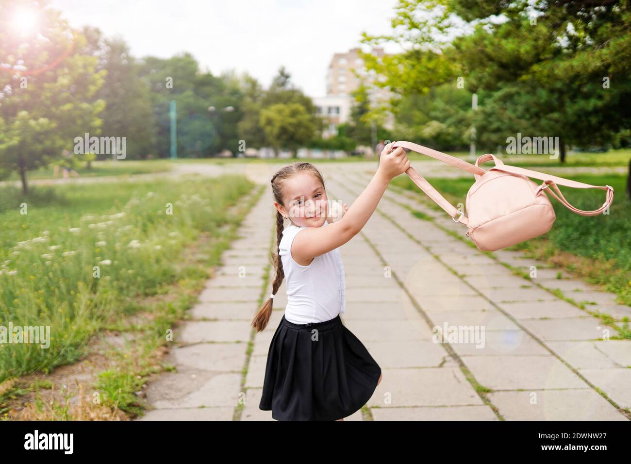 A little smiling school girl with pigtails throwing her bagpack in school yard Stock Photo