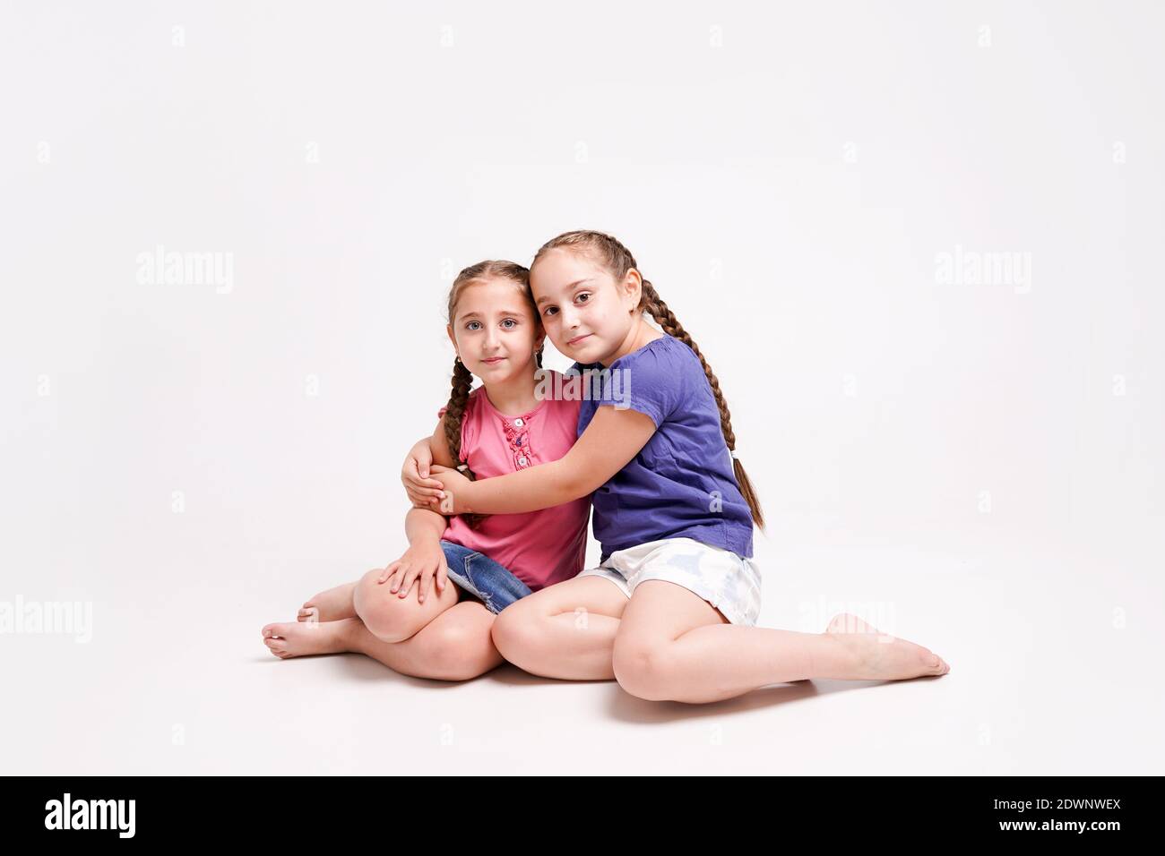 Fun girls, sisters sitting on the floor on their knees and hugging on white background Stock Photo