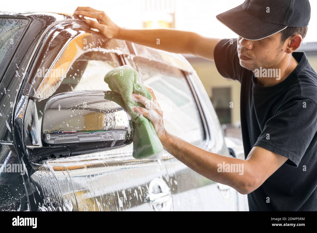 Car wash worker wearing a Tshirt and a black cap is using a sponge to