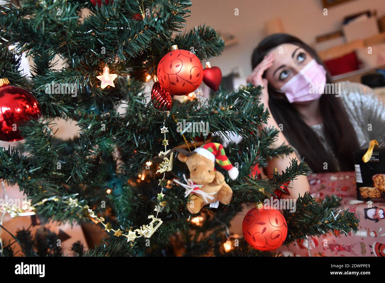 Topic picture lonely Weihafterts 2020 in the coronavirus pandemic. A young woman with face mask, mask sits alone behind her Weihaftertsbaum on Christmas Eve and looks at and looks at gifts. Pandemic, lockdown, shutdown, incidence value. MODEL RELEASED! | usage worldwide Stock Photo
