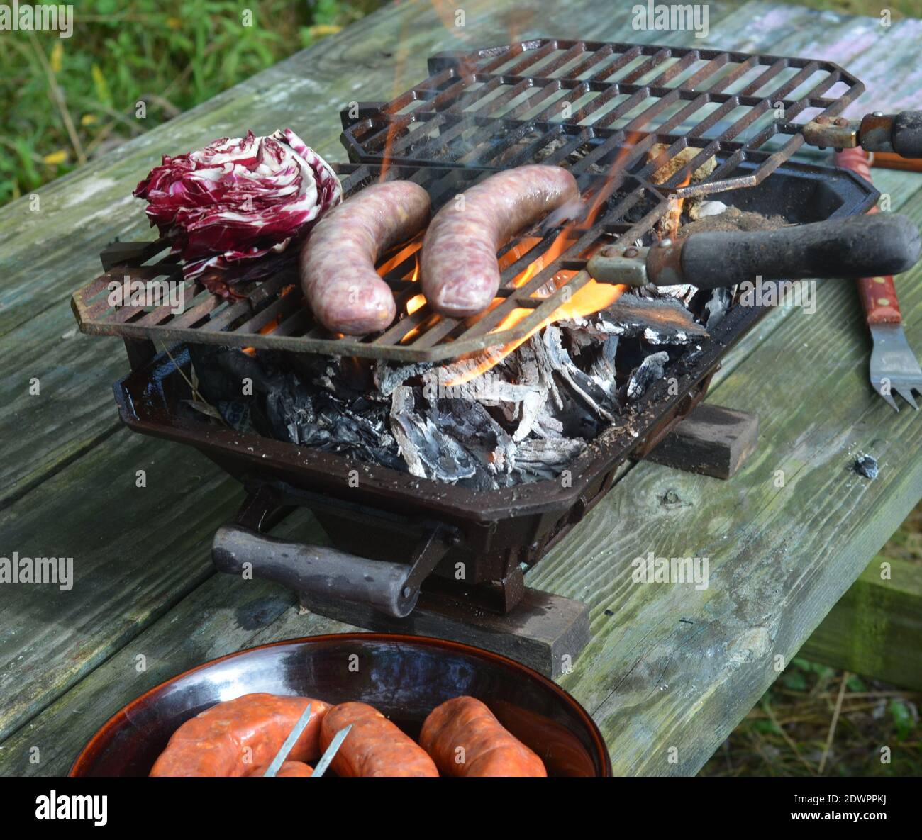 Hibachi Tabletop Grill On Picnic Table, Flames, Brats, Radicchio, Italian Sausages Stock Photo