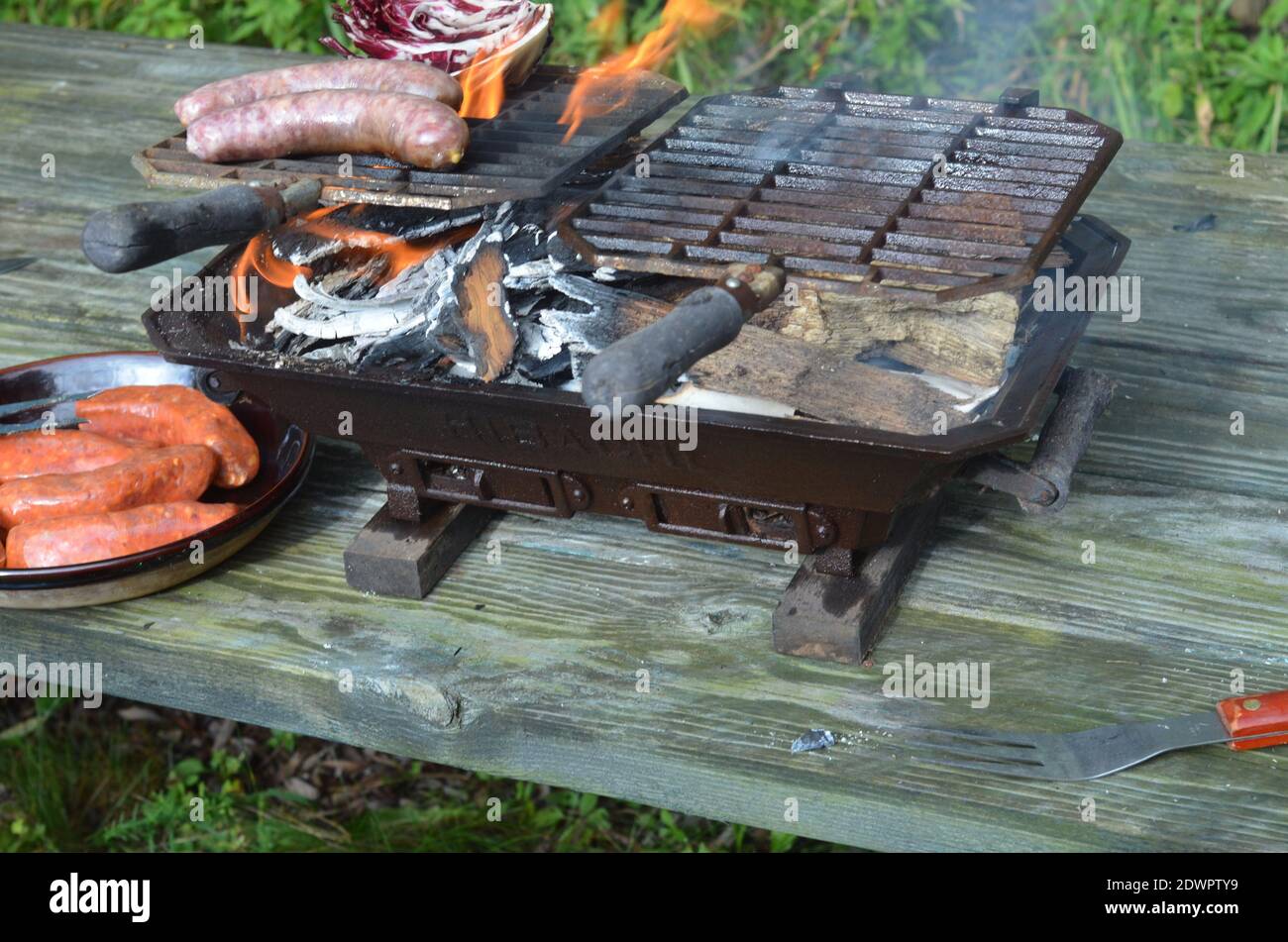 Hibachi Tabletop Grill On Picnic Table, Flames, Brats, Radicchio, Italian Sausages Stock Photo