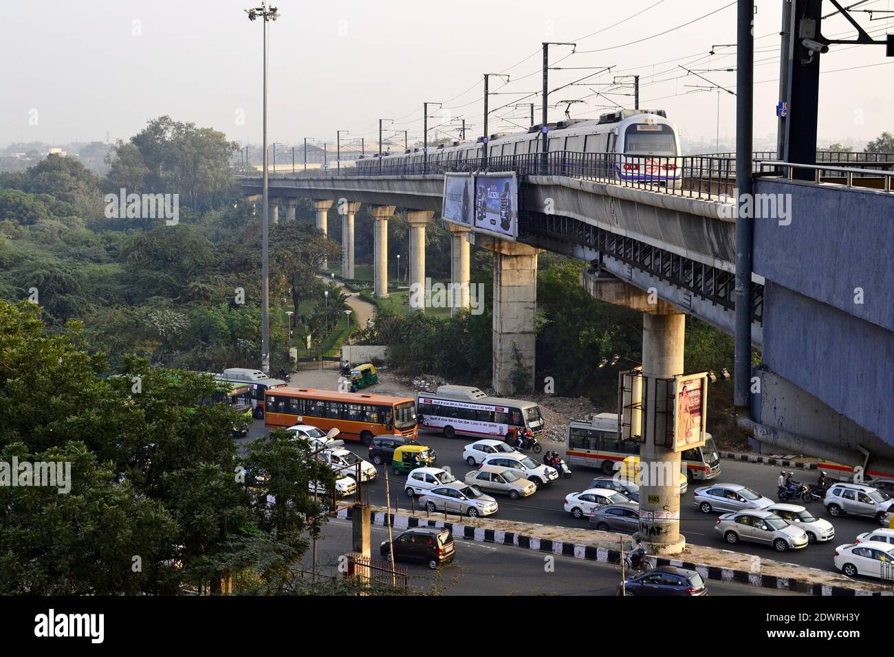 Delhi, India - October, 2016: Delhi metro train on the railway concrete bridge and traffic jam on the road below in the evening Stock Photo