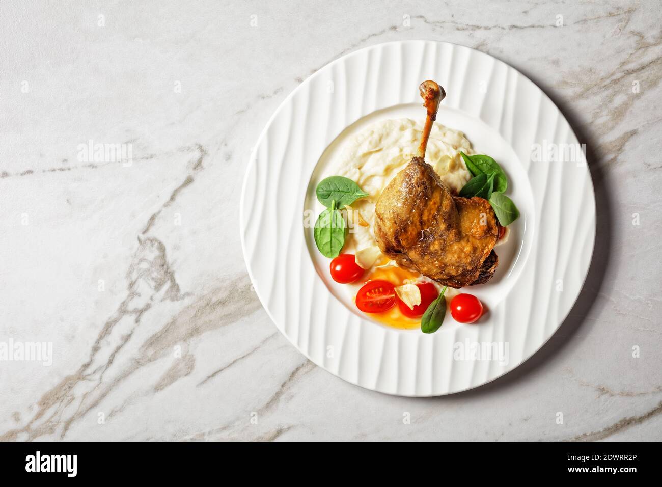 French cuisine roasted duck leg - duck confit with parsnip puree and orange sauce, with fresh spinach leaves served on a white plate on a white marble Stock Photo