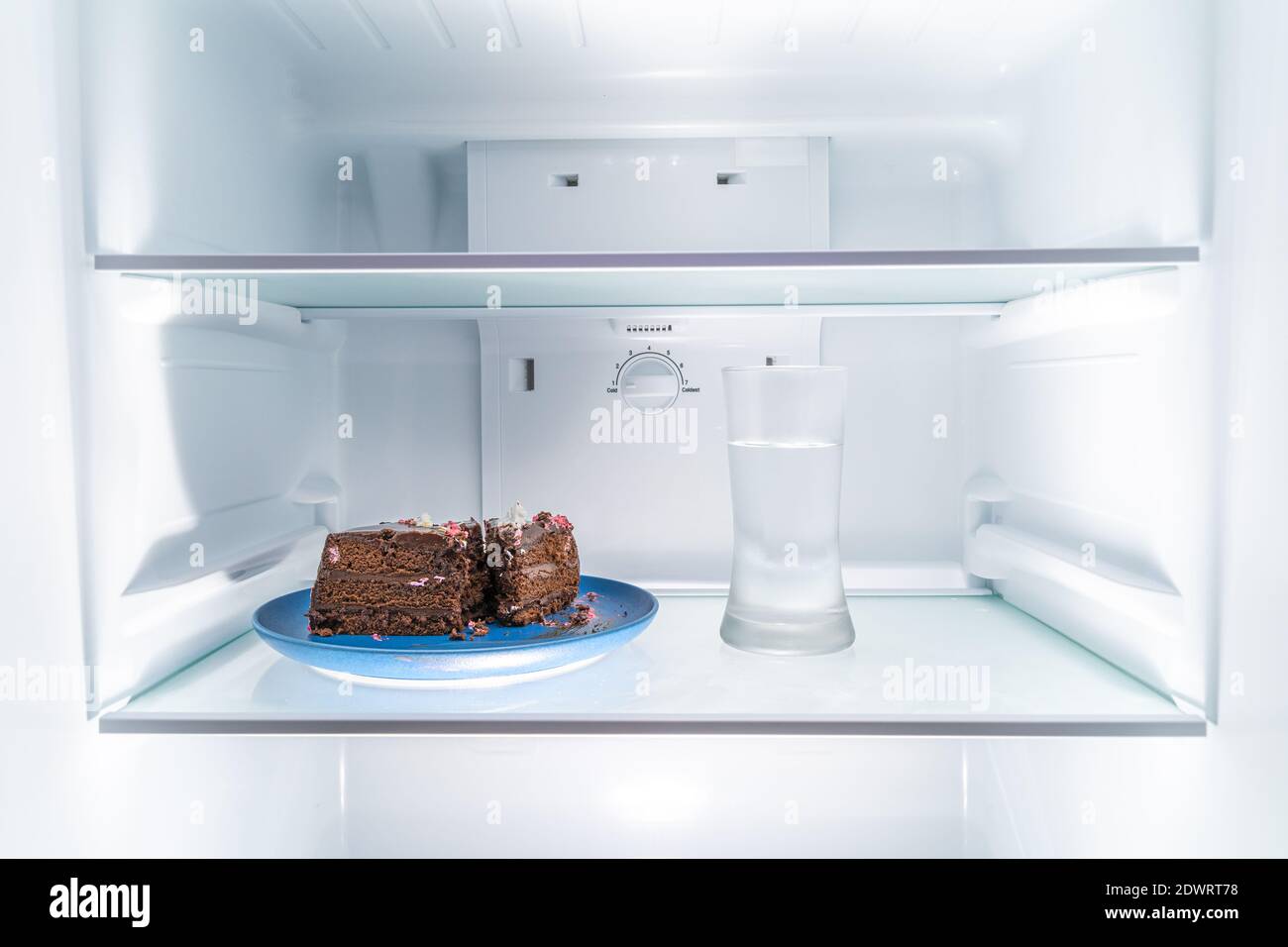 Chocolate cake on a blue plate and a glass of water placed in a clean refridgerator, diet or food concept Stock Photo