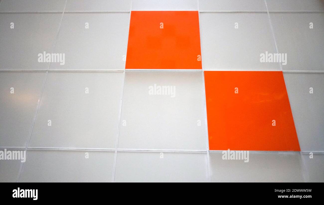 A white wall with an orange tile. Selective focus Stock Photo