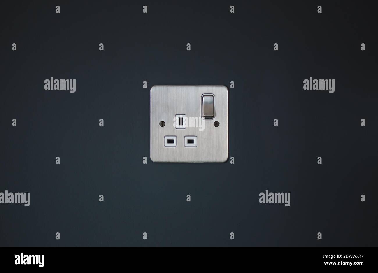 Silver UK mains electricity plug socket in dark grey wall Stock Photo