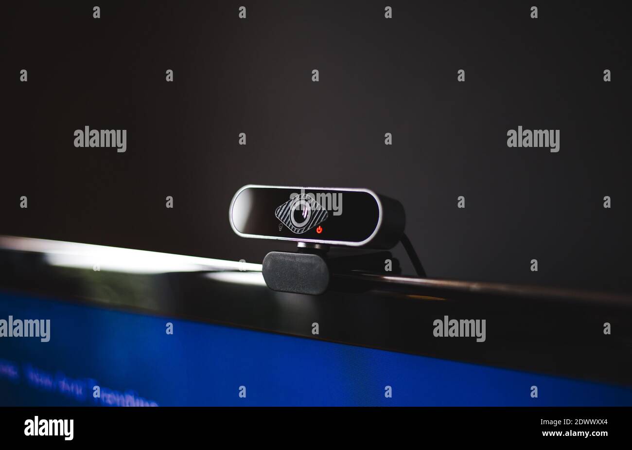 Black webcam clipped onto the screen of a TV or computer monitor with dark gray background and red light on recording video call Stock Photo