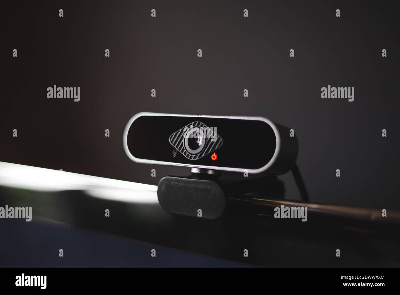 Black webcam clipped onto the screen of a TV or computer monitor with dark gray background and red light on recording video call Stock Photo