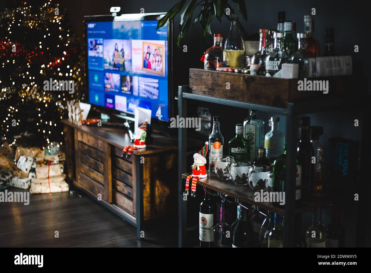 Santa toy sits on the shelf of a drinks trolley in a cozy, festive living room of a dark grey apartment ready for Christmas Stock Photo
