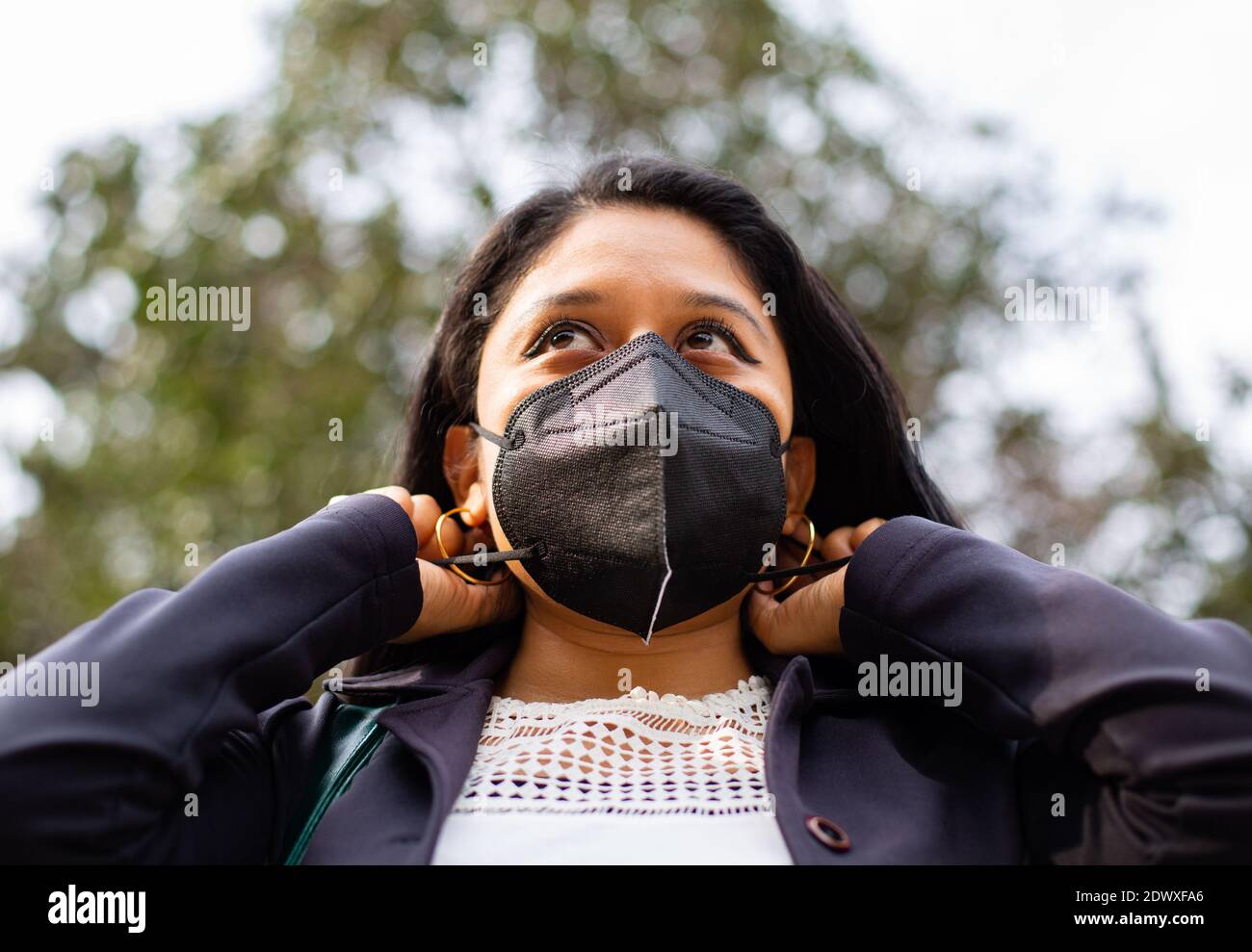Close-up of Latin businesswoman wearing a face mask for protective reasons during the covid 19 pandemic. She is putting on a mask Stock Photo