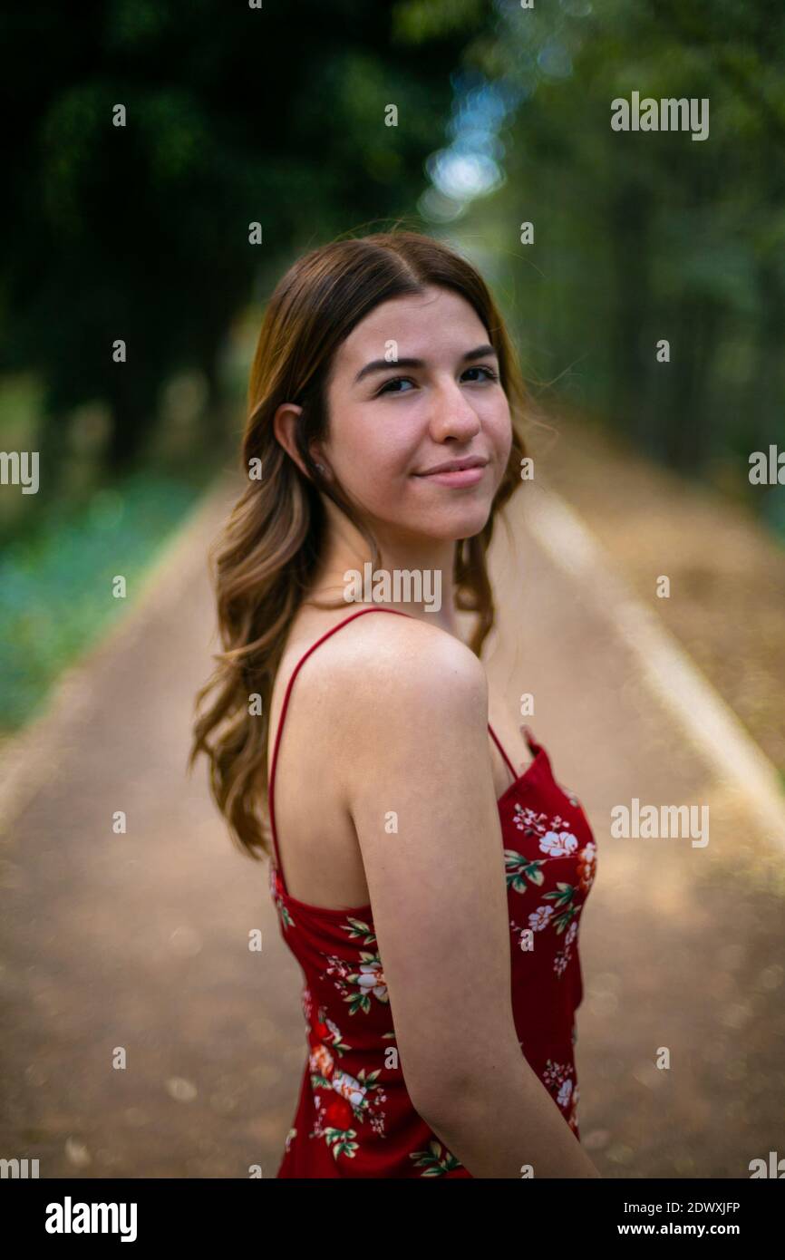 Portrait of a young woman in a park, She wears a red dress. She is