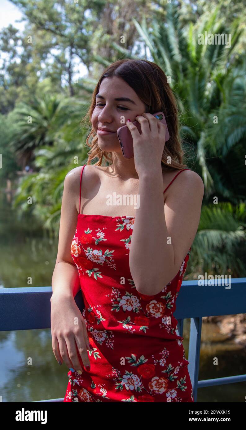 Beautiful young woman wears a red dress. She is talking on the phone in the park Stock Photo