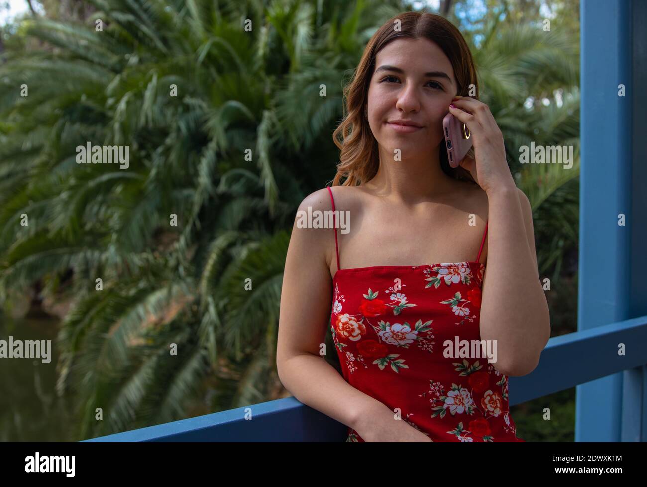 Beautiful young woman wears a red dress. She is talking on the phone in the park Stock Photo