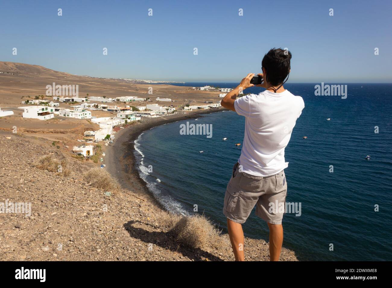 Young man standing on cliff edge to take photo of Puerto Calero coast ...