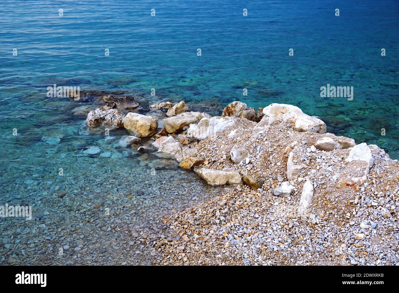 Stone reef and pebbles immersed in the clear blue sea water Stock Photo