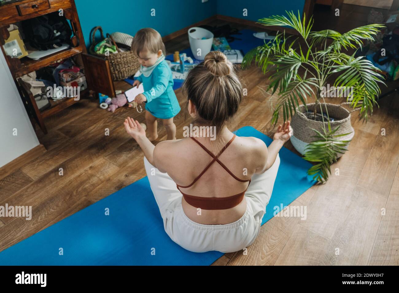 Young mother sitting on the floor, enjoy meditation do yoga exercise at home with his little daughter baby girl. Mental health, self care, No stress Stock Photo