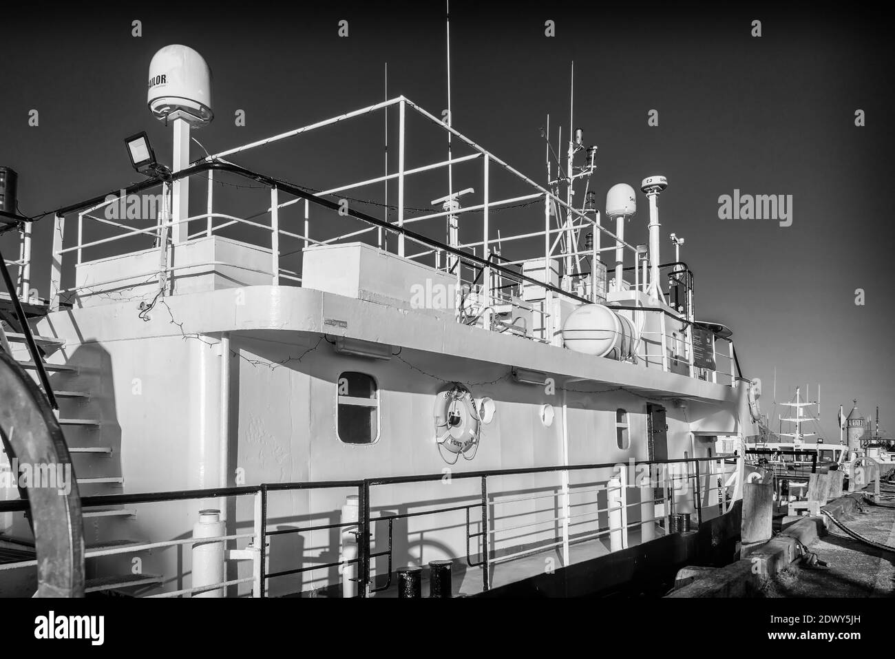 A boat moored in a harbour with a the light from a low sun onto its starboard side.  The upper deck bristles with antenna and radar. Stock Photo