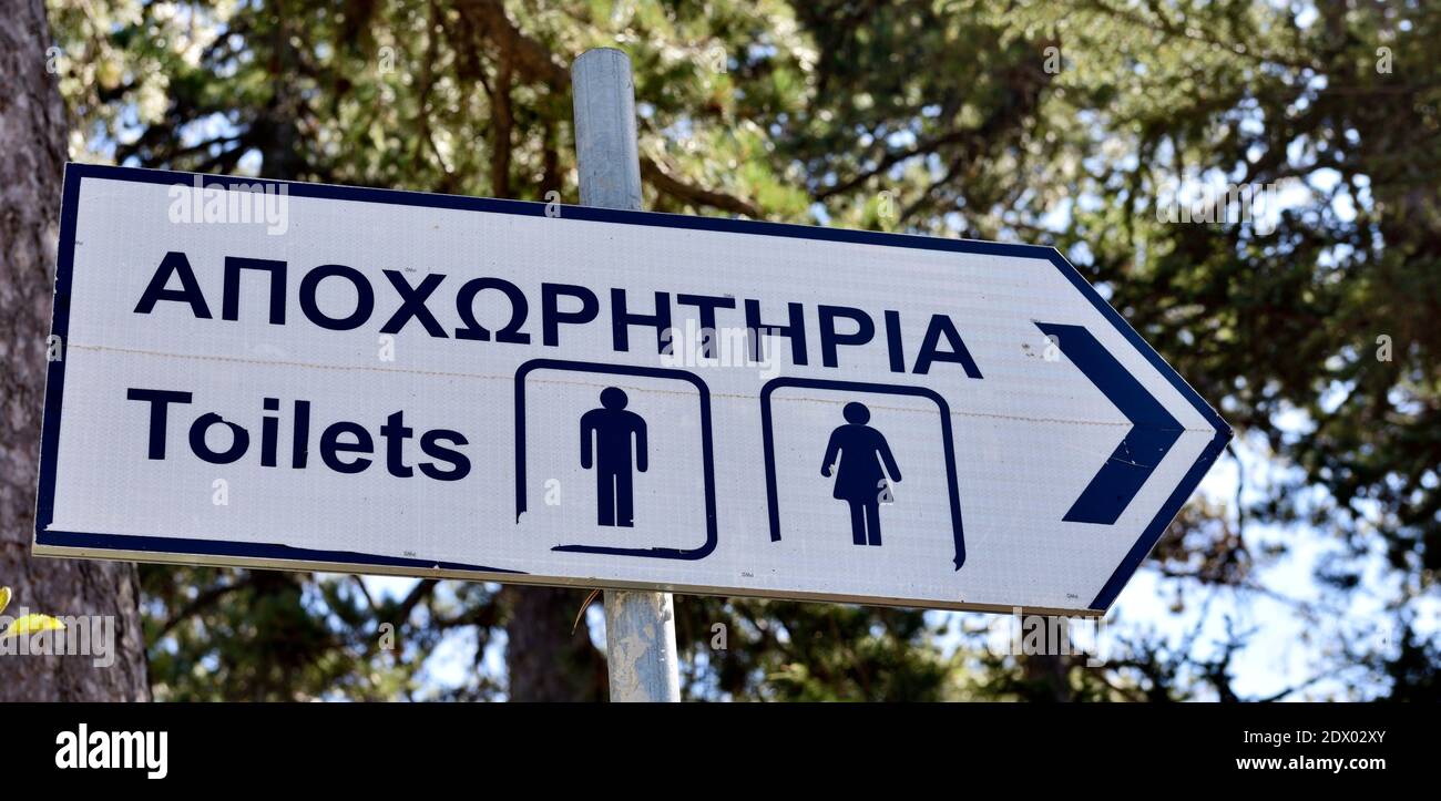 Sign pointing to location with toilets in English and Greek with men and woman symbol Stock Photo