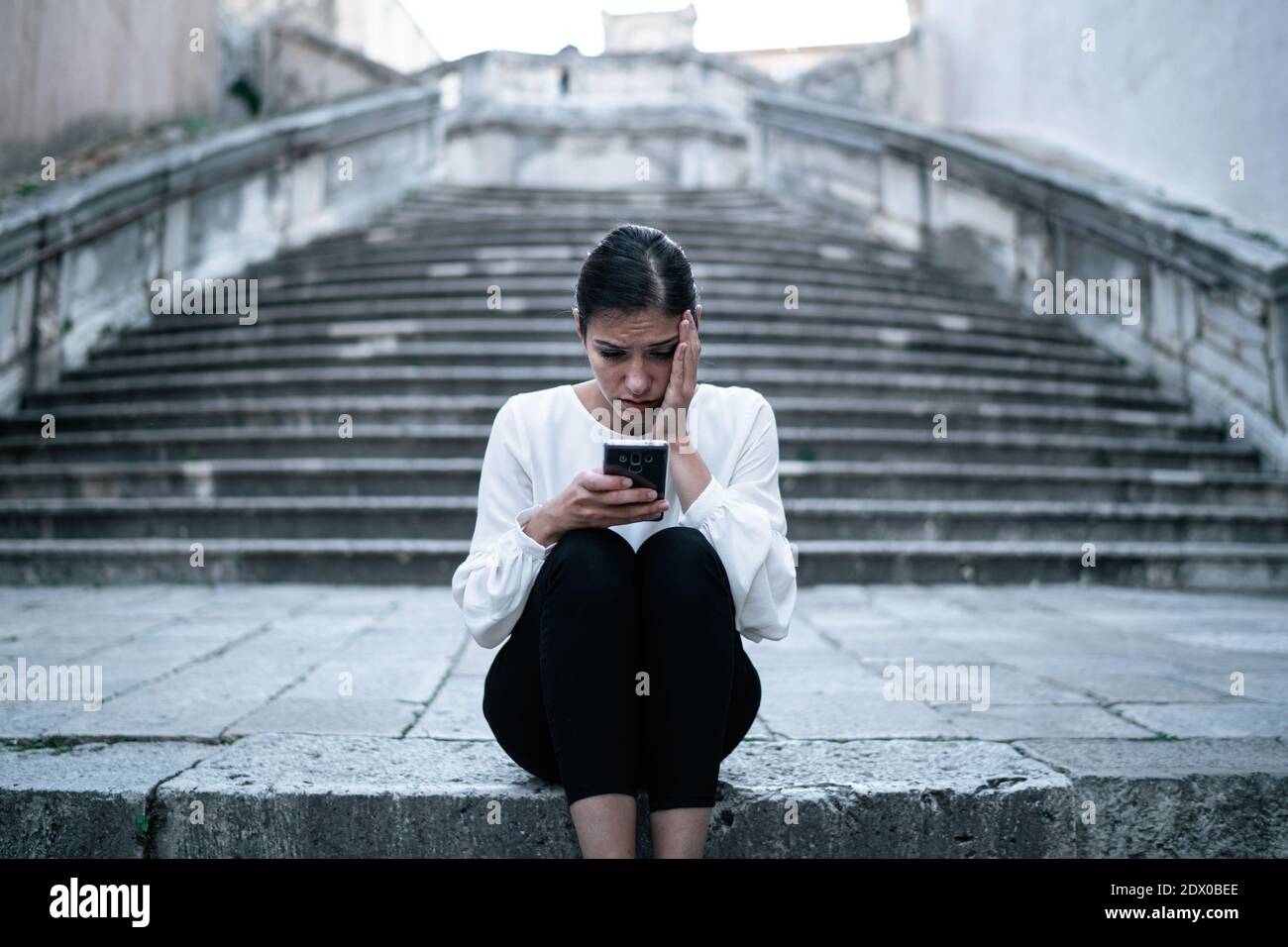 Depressed woman reading a bad news message on the smartphone.Coronavirus panic news.A shocking internet headline.Looking for illness symptoms.Negative Stock Photo