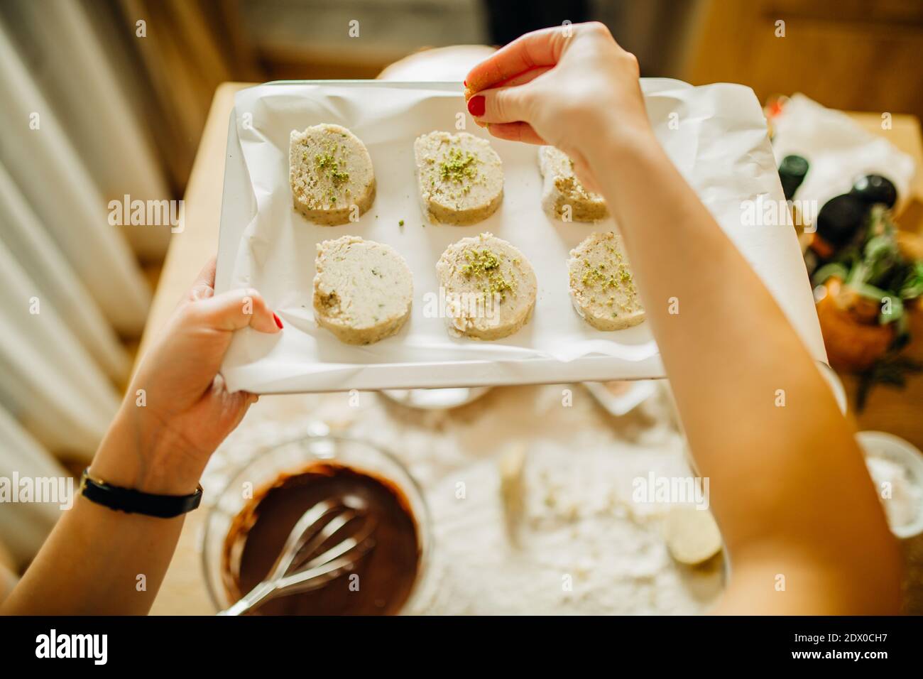 Housewife making finishing touches on vanilla pistachio cookie biscuits.Woman making a homemade dessert with an easy recipe, sprinkling ground nuts on Stock Photo