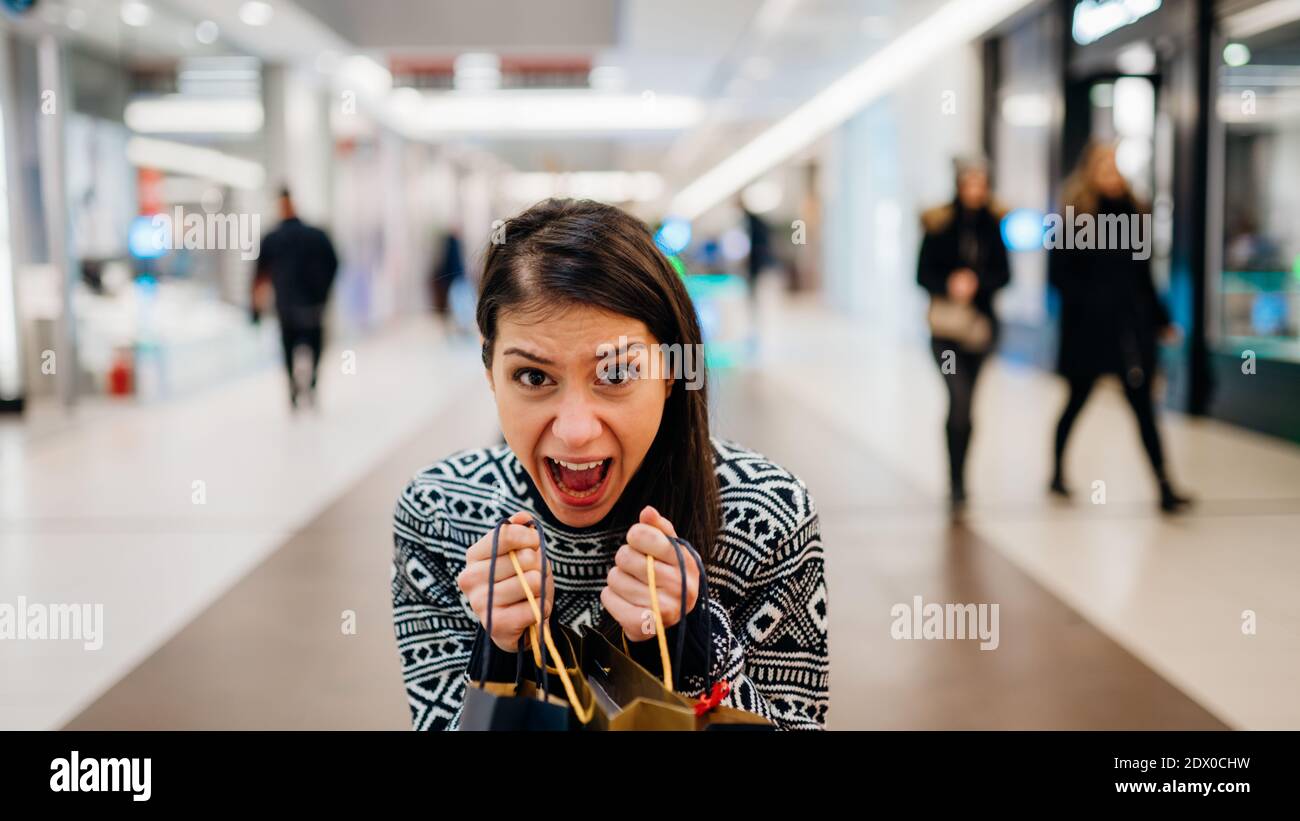 Excited female shopper holding bought items in colourful bags.Customer in a shopping mall, discount prices shopping craze.Woman addicted to shopping b Stock Photo