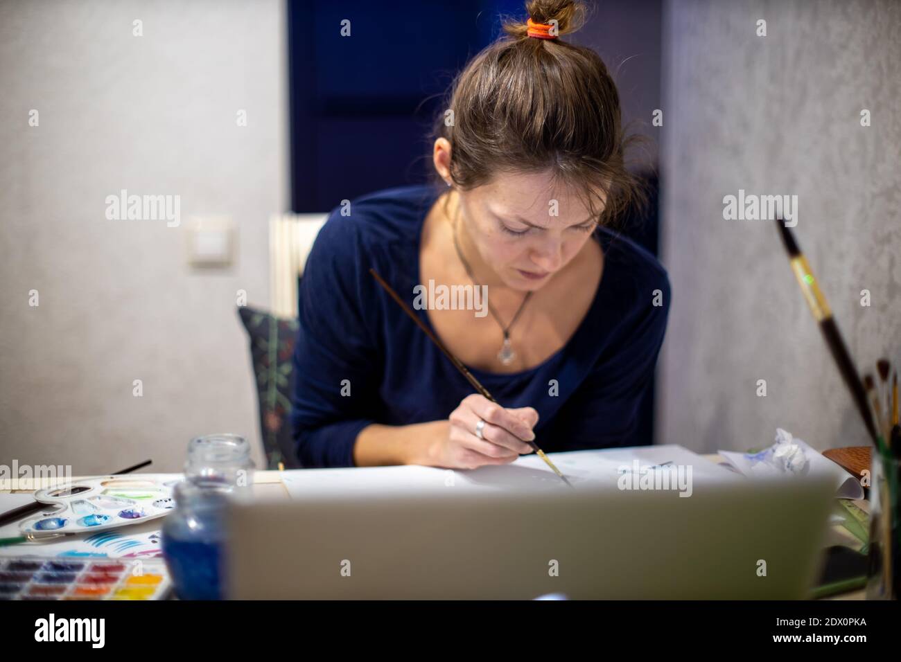 Portrait of creative young woman seated at table in an artists' workshop, working on painting Stock Photo