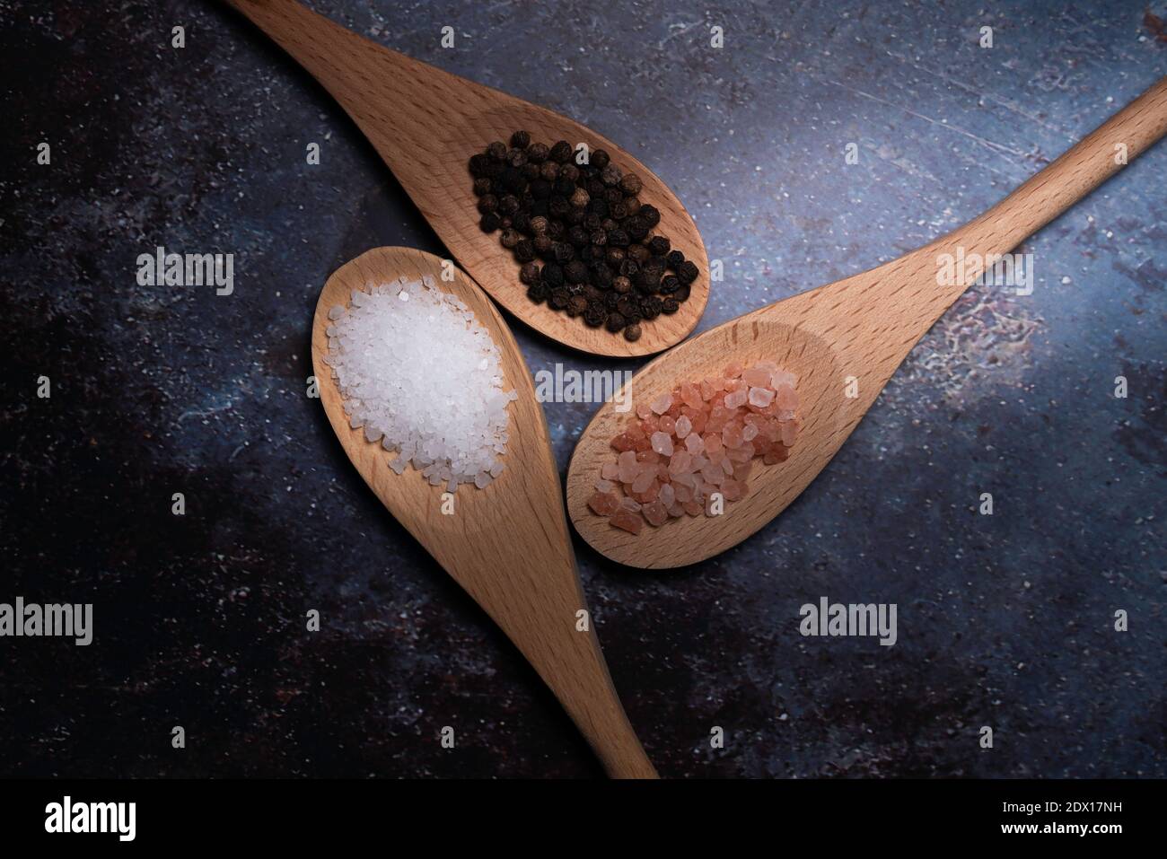 Directional Lighting on three wooden spoons with black peppercorns, White Kosher Salt, and Pink Sea Salt Stock Photo