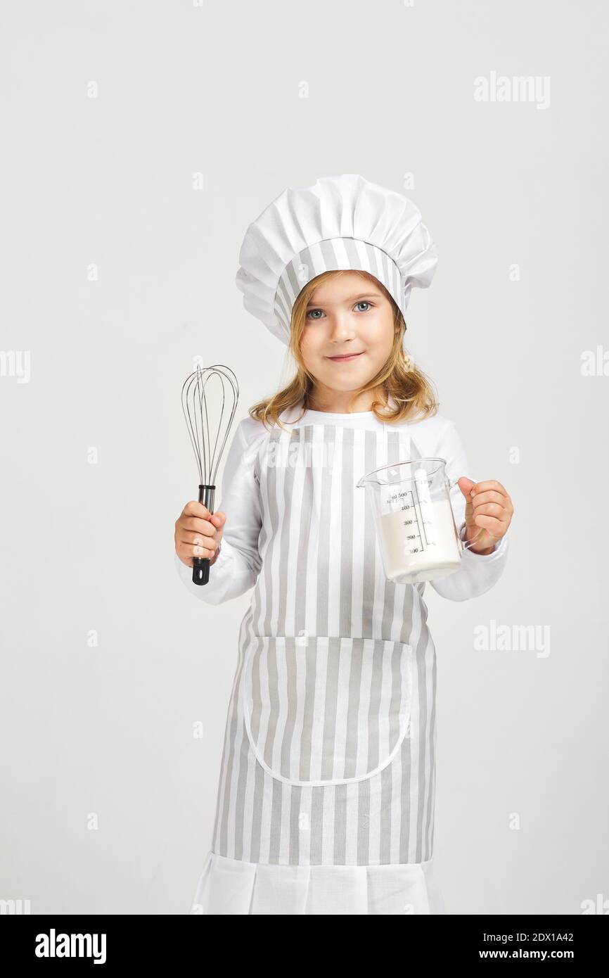 little girl in chef hat and apron with flour in measuring cup and whisk