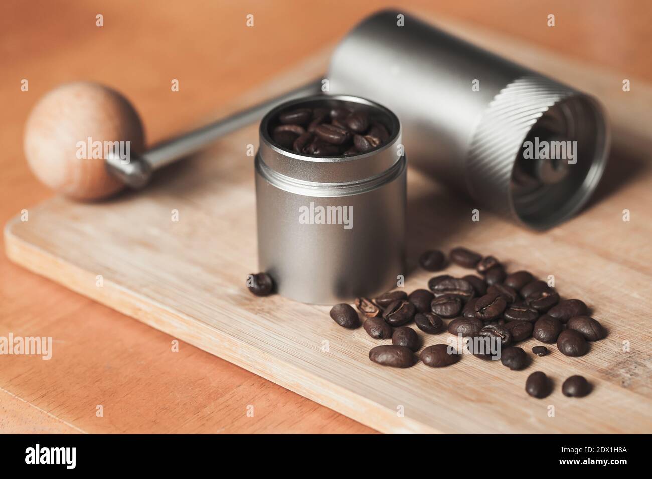 Manual coffee grinder and dark roasted coffee beans are on wooden desk, close-up photo with selective soft focus Stock Photo