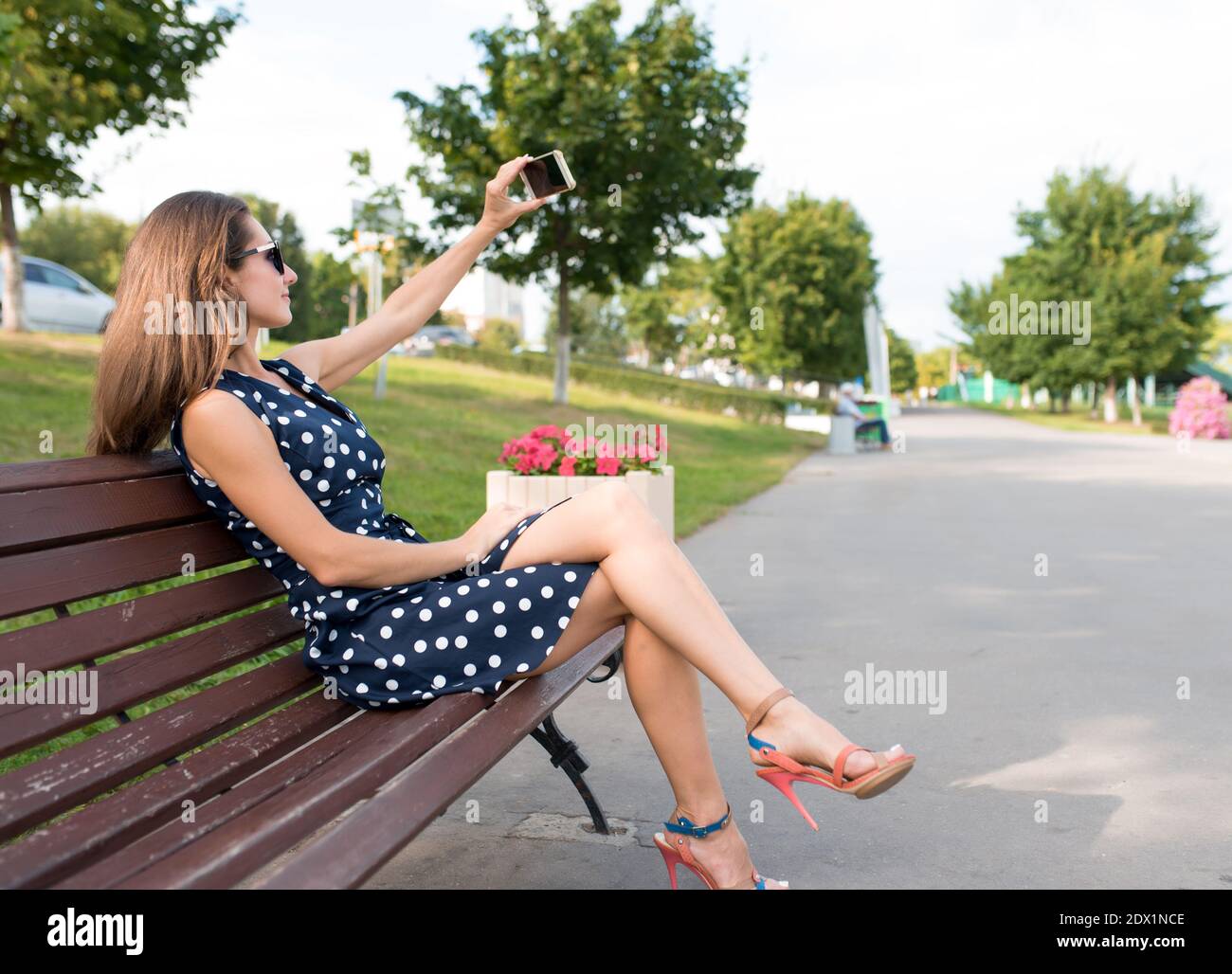 woman in dress, summer city sits on bench takes selfie of herself  smartphone. In his hand phone, video call video recording. Long hair,  background Stock Photo - Alamy