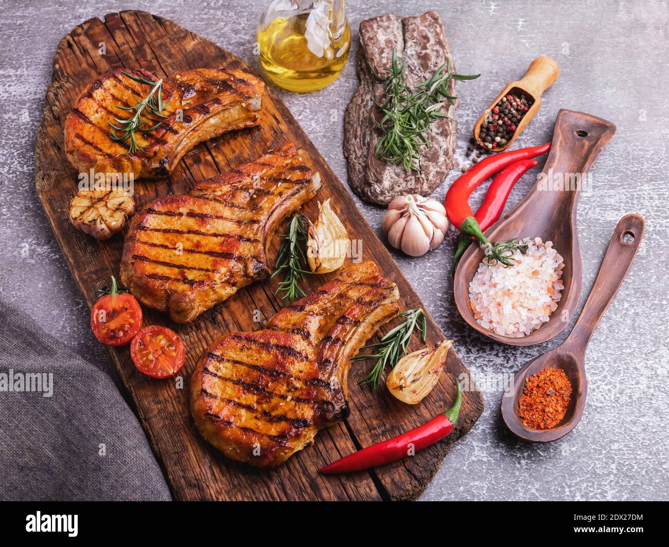 cooked grilled meat pork, beef, chop bone, cutting board, spices, tomato, rosemary Stock Photo