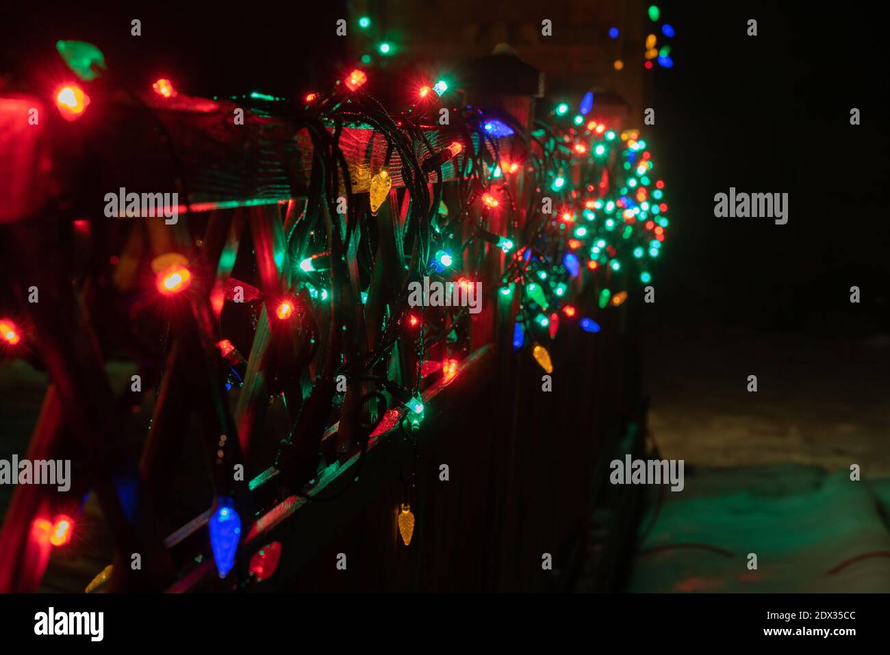 Real blurry Christmas Multicolored Lights on wooden terrace fence. Many flashing lamps that sequentially changes color. New year and Christmas decorat Stock Photo