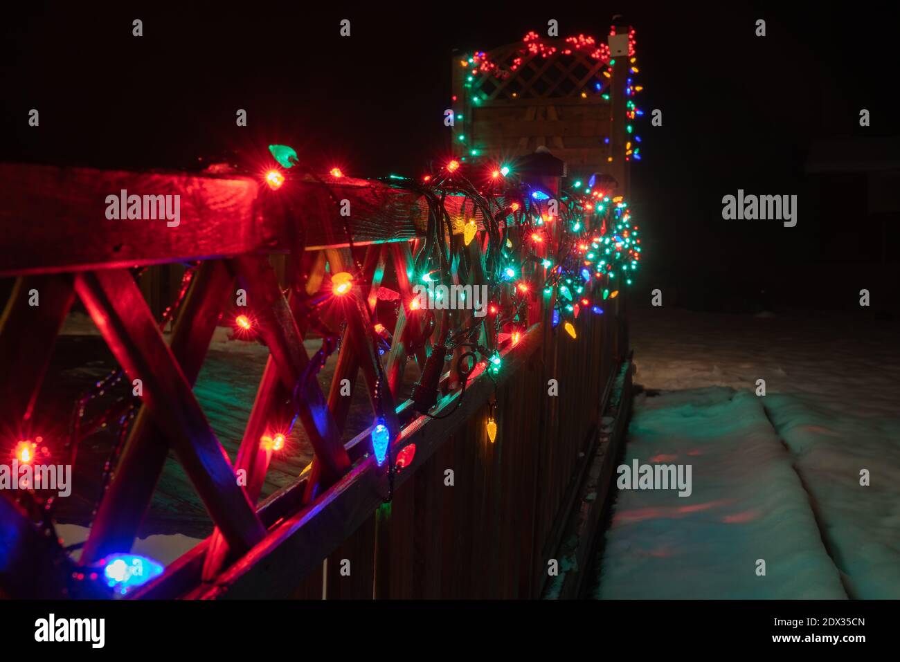 Perspective view of Real blurry Christmas Multicolored Lights on wooden terrace fence. Many flashing lamps that sequentially changes color. New year a Stock Photo